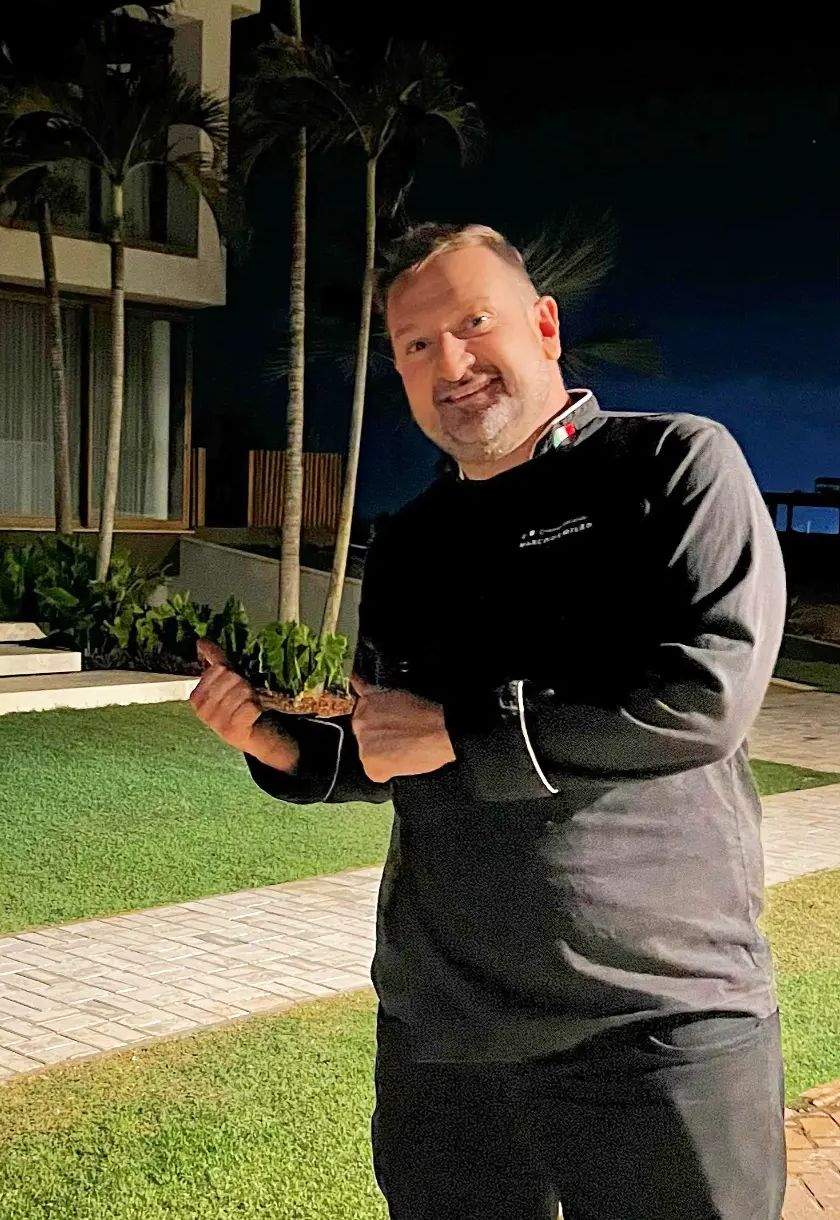 Chef Marco de Milão, de dólmã escura, no jardim de uma casa à noite antes de um jantar
